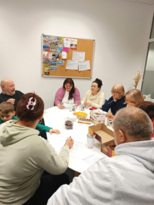 Menschen jeden Alters sitzen um einen Tisch mit Snacks und üben ihre Sprachkenntnisse