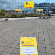 J. Kemnitz hält ihr Namensschild für den Fürsorgetag. Im Hintergrund ist der Eingang der Messe zu sehen